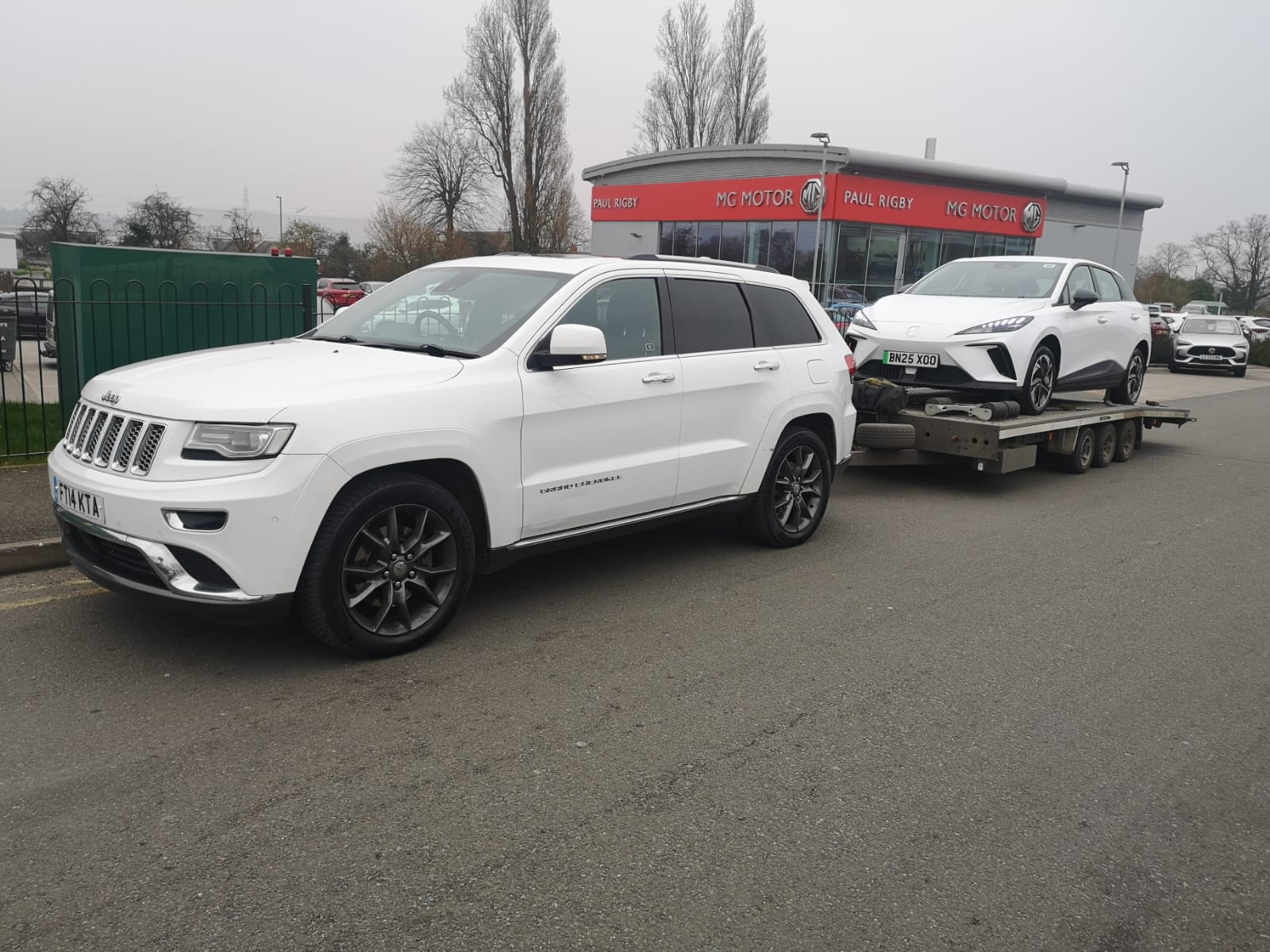 Jeep Grand Cherokee towing MG vehicle outside dealership