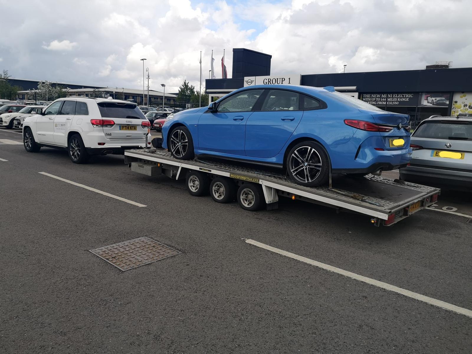 Blue BMW sedan on flatbed trailer at dealership